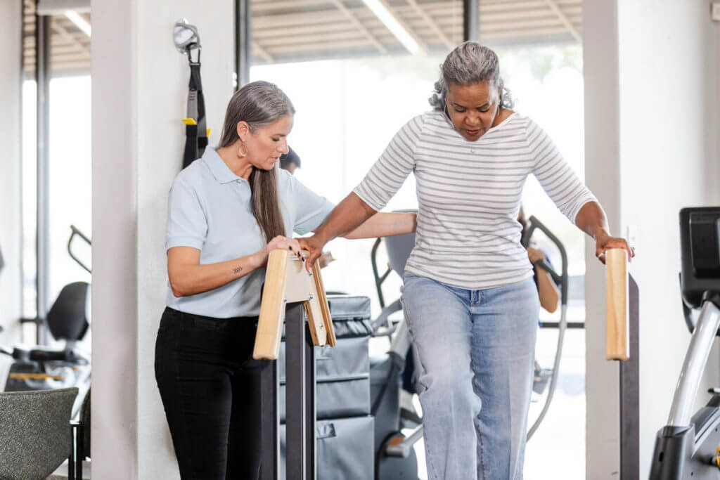 Mature female patient carefully walks down stairs at physical therapy clinic