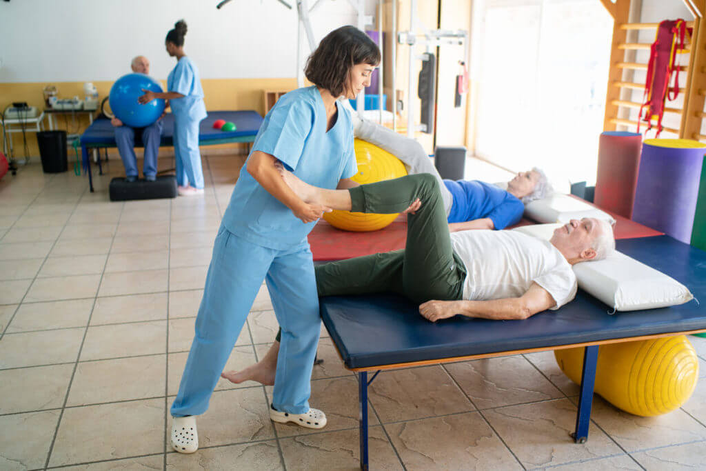 A nurse is assisting a senior man with leg exercises at knee and hip rehab.