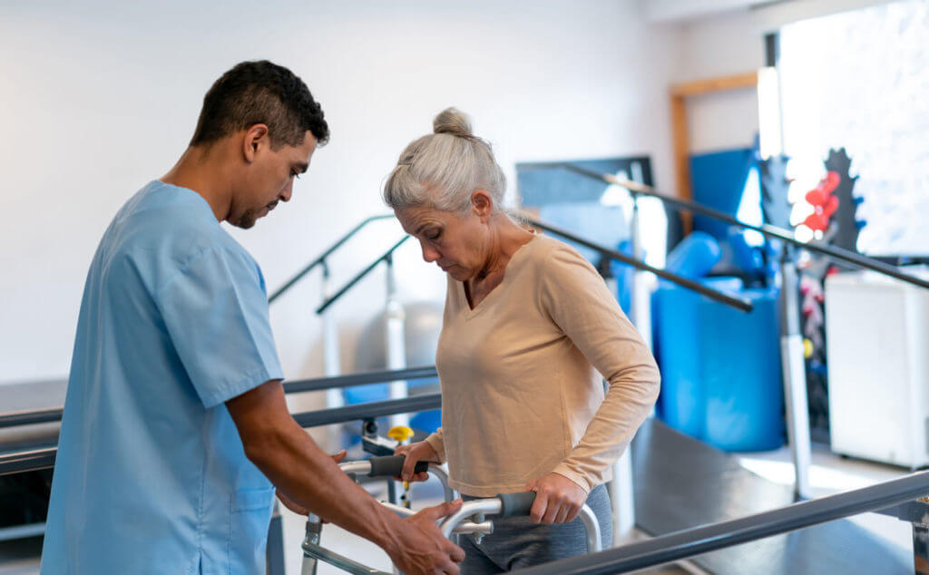 Male therapist helping a senior female patient use a walking frame during physical therapy.