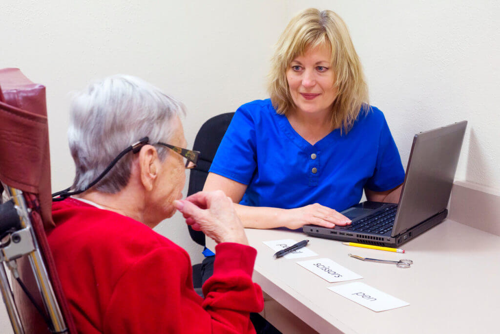 An elderly woman is undergoing speech therapy with a specialist.