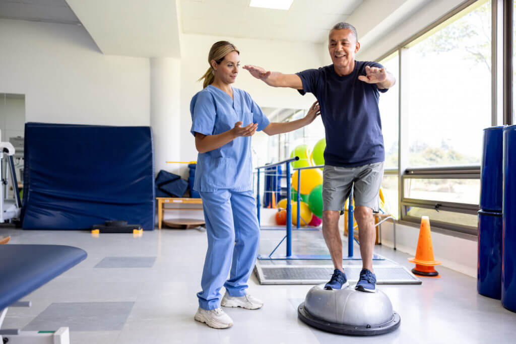 Man balancing on a flat bottomed yoga ball as part of his vestibular therapy program.